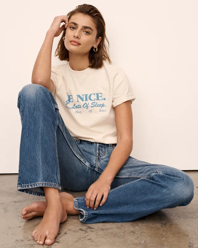 Taylor Hill sitting barefoot on the floor wearing jeans and a white T-shirt.