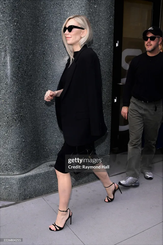 Vanessa Kirby walking outside in a black outfit and black heels.