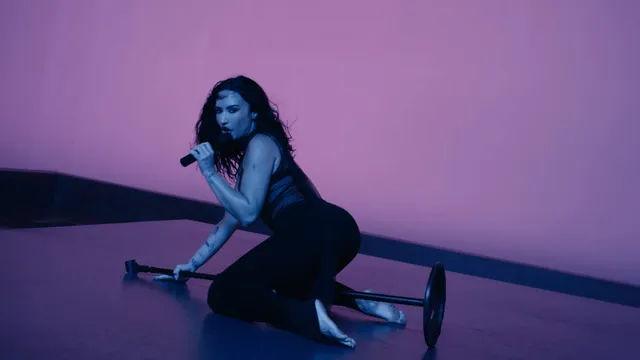 Demi Lovato performing barefoot in a purple-lit studio setting.