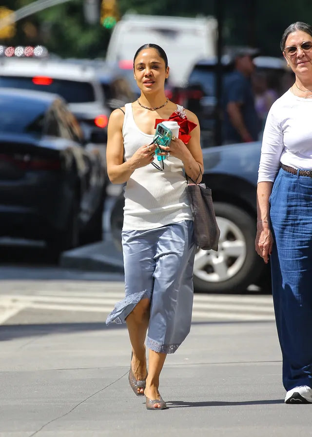 Tessa Thompson walking outside carrying a drink.