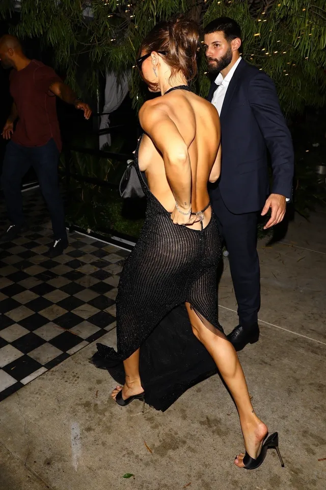 Hailey Bieber walking outdoors in a black dress and heels.