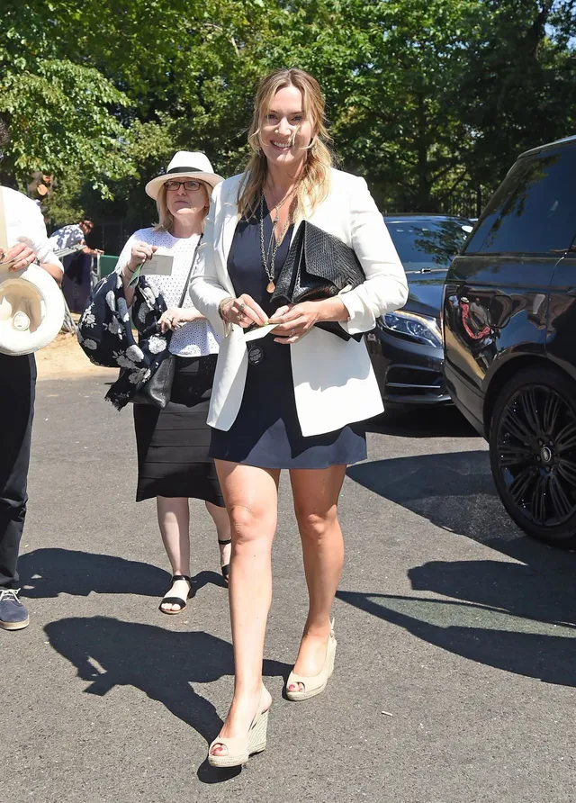 Kate Winslet walking outdoors in a white jacket and heels.