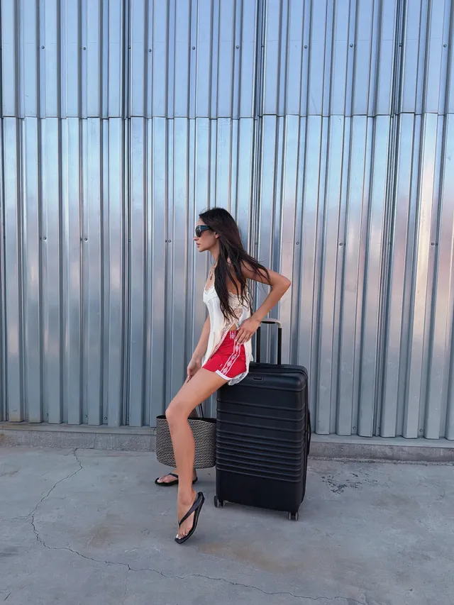 Shay Mitchell sitting on a suitcase in flip-flops.