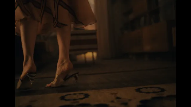 Emilia Clarke walking across a wooden floor in strappy heels.