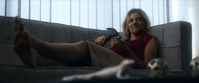 Samara Weaving reclining barefoot on a sofa in a film scene.