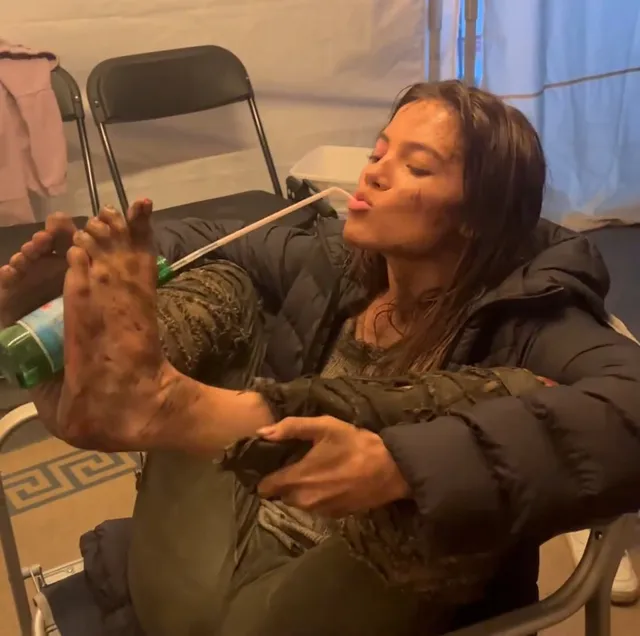 Freya Allan raising her bare feet while sitting on a film set.