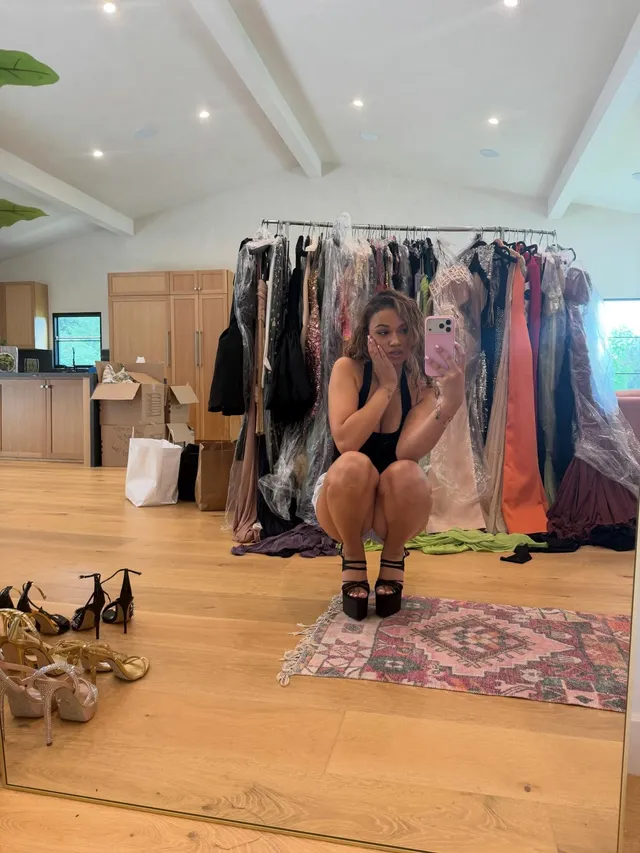 Madison Bailey crouching in a dressing room wearing black platform heels.