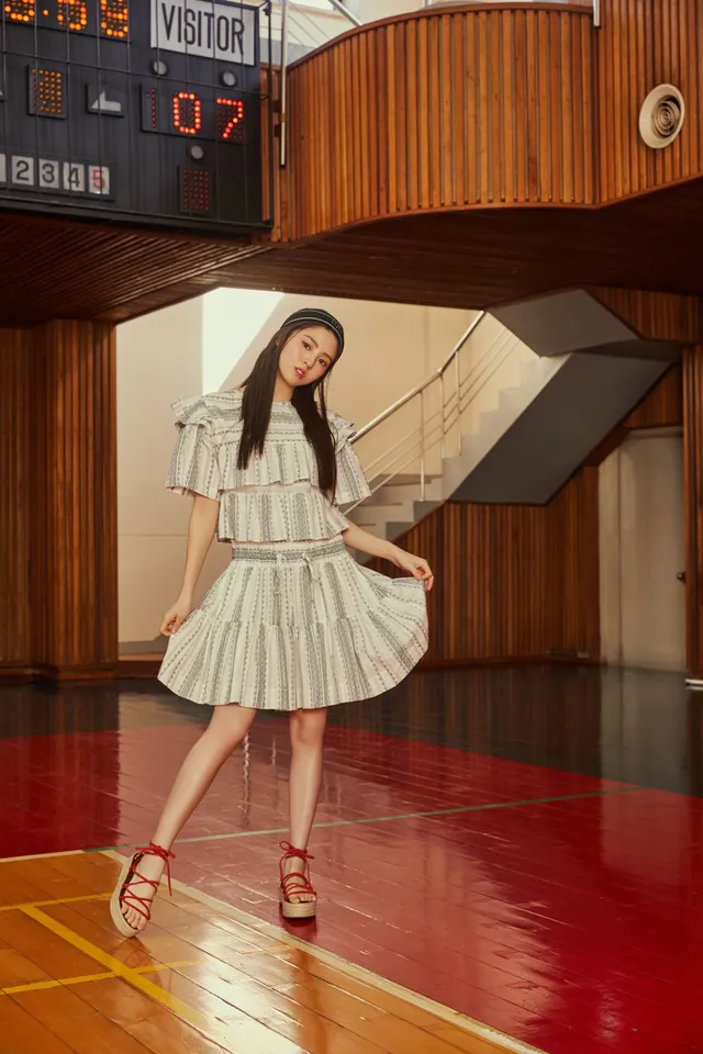 Han So-hee wearing a light dress and flat sandals indoors.