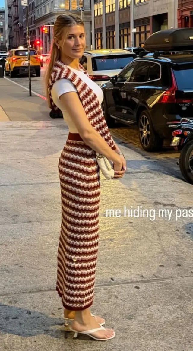 Eugenie Bouchard standing in flat sandals and a striped dress on a pavement.