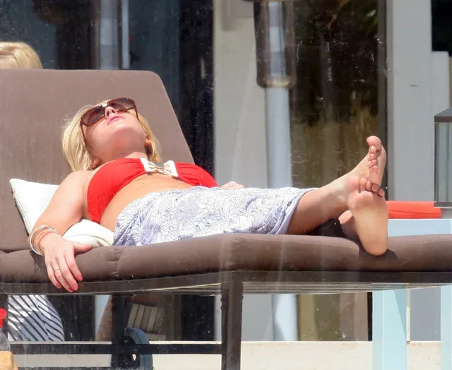 Lindsay Lohan reclining barefoot on a sun lounger in a red top.