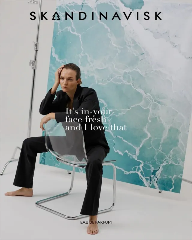 Josephine Skriver sitting barefoot in a black outfit during a fragrance shoot.