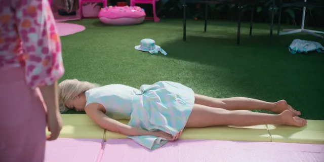 Margot Robbie lying barefoot on a lawn in a colorful film scene.
