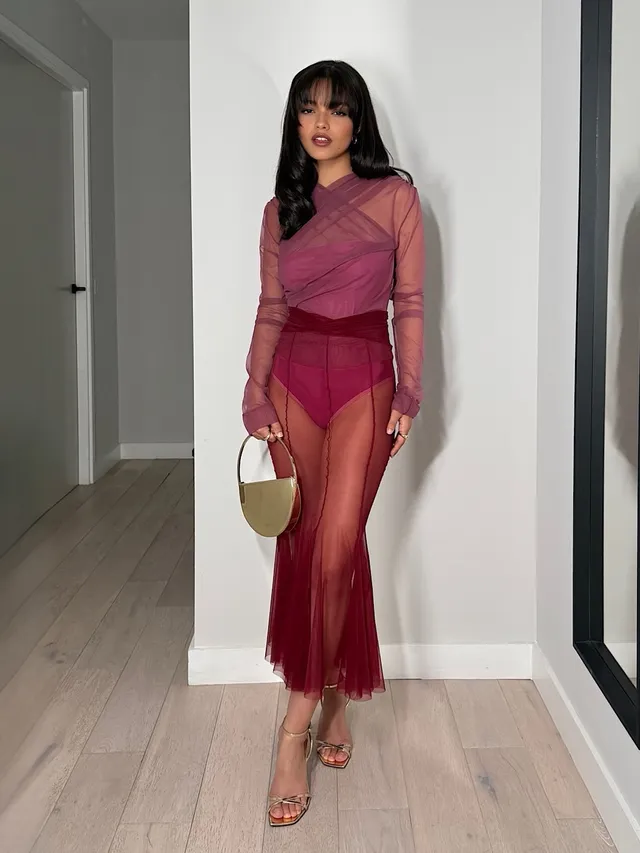 Rachel Zegler standing in a sheer red dress and metallic heels.