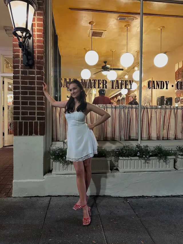 Lola Tung standing outside a shop in a pale dress and pink heels.