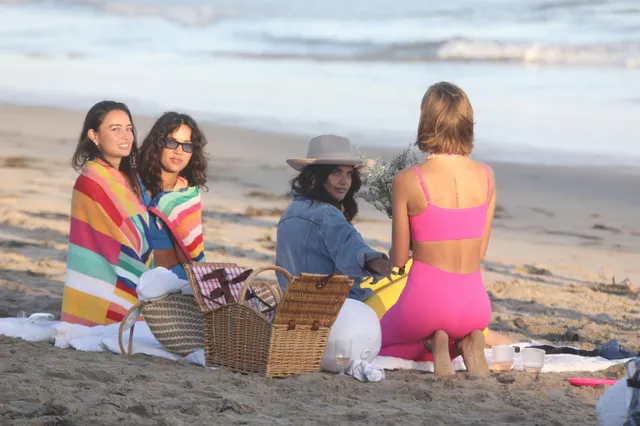 Josephine Skriver kneeling barefoot on a beach with companions.