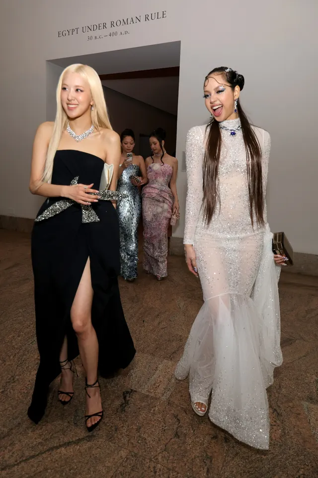 Lisa (Lalisa Manobal) walking with a companion in black heels and a dark dress at an evening event.