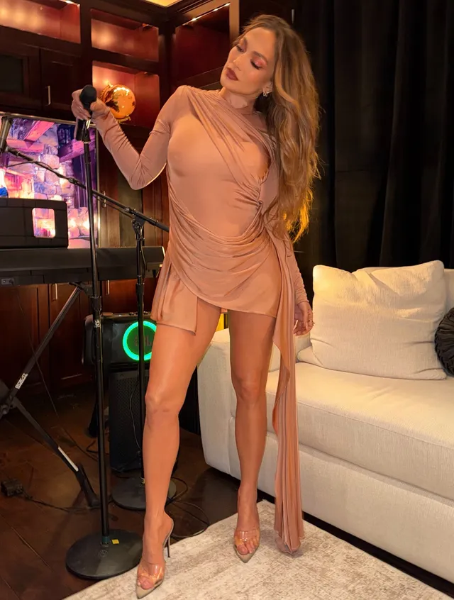 Jennifer Lopez a tan dress and clear heels beside a microphone.