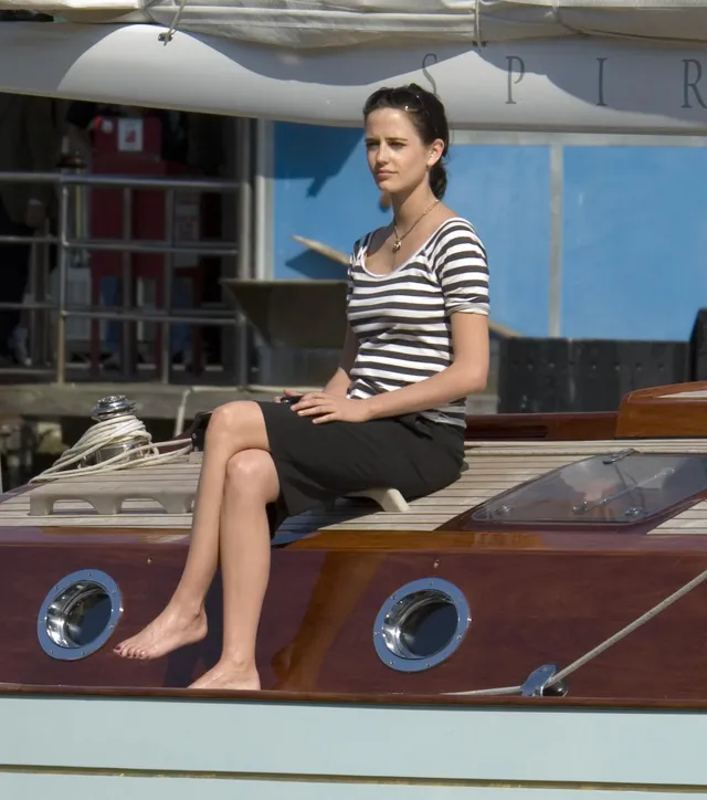 Eva Green seated on a wooden boat in a striped shirt.
