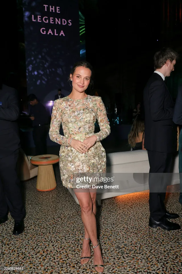 Alicia Vikander posing at a gala in an embellished pale dress.