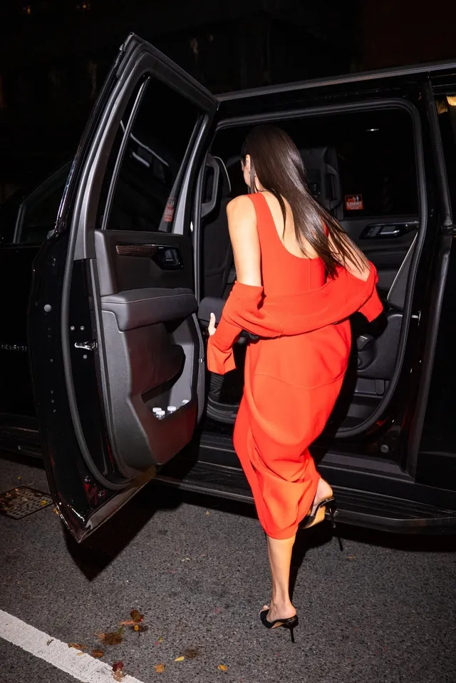 Nina Dobrev stepping from a vehicle in a red outfit and black heels.