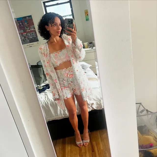 Kiana Madeira taking a mirror selfie in a pale floral skirt set and heels.