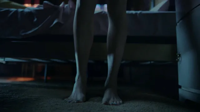 Peyton List standing barefoot on a dark carpet in a scene.