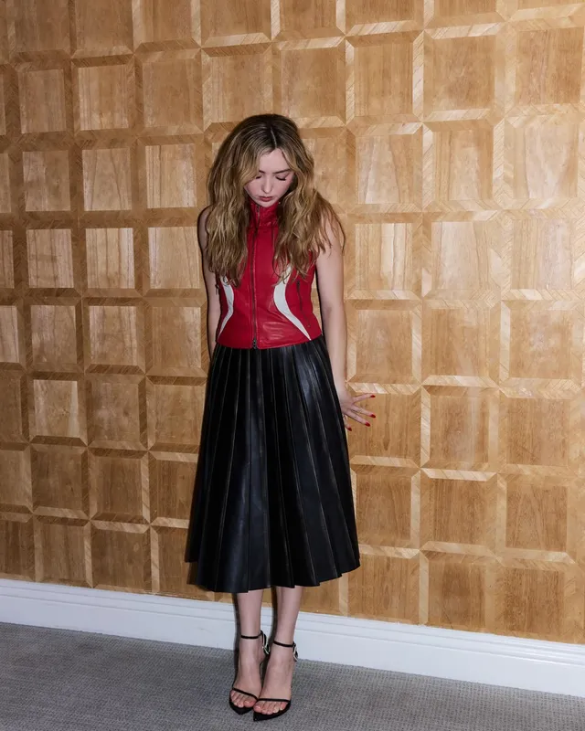 Peyton List posing in a red top and black ankle-strap heels.