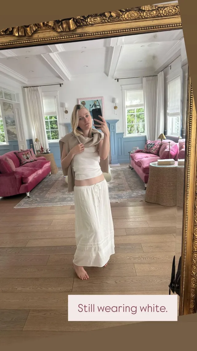 Dakota Fanning standing barefoot in a white outfit for a mirror photograph.