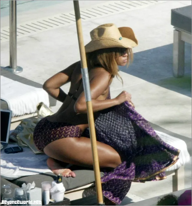 Beyoncé kneeling barefoot beside a pool wearing a sun hat.