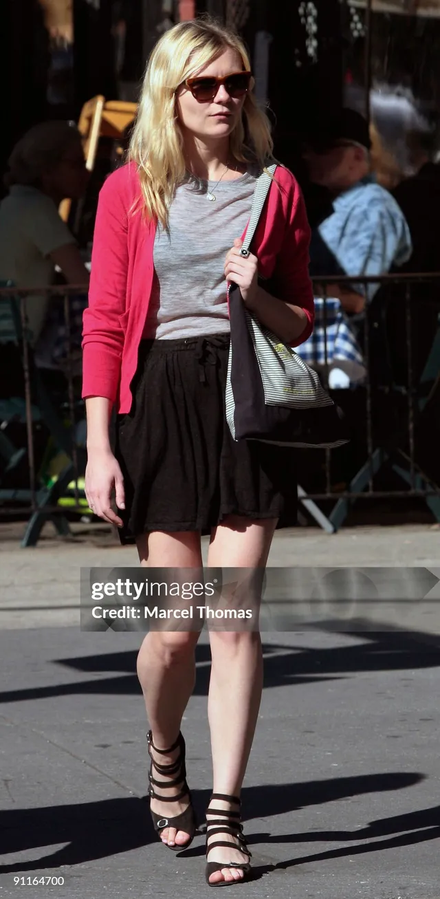 Kirsten Dunst walking in a red cardigan and dark skirt.