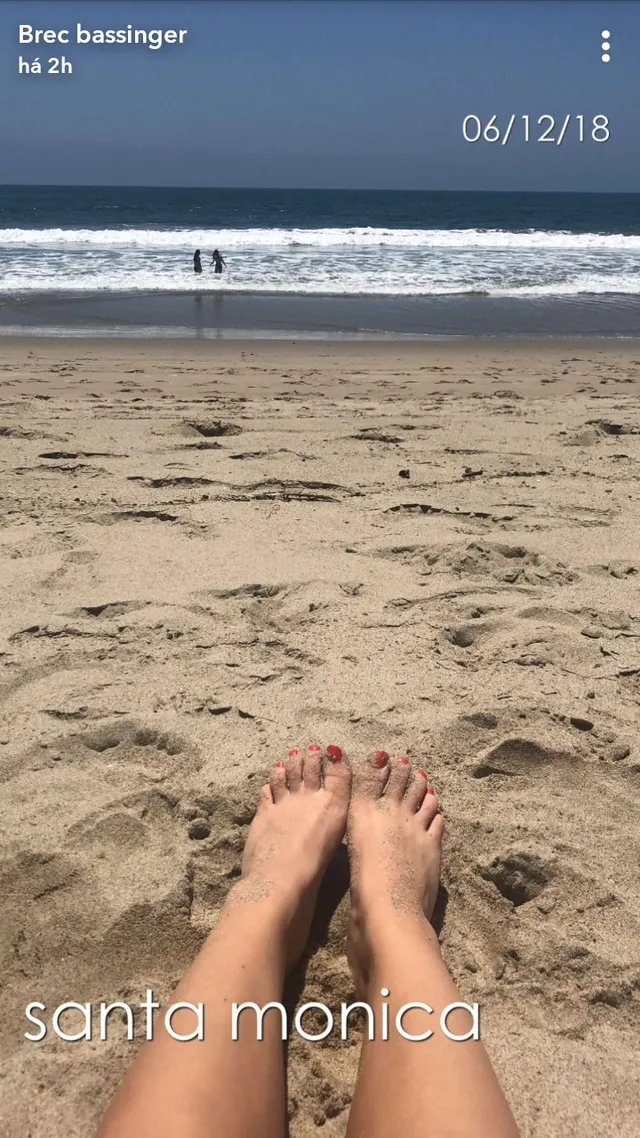 Brec Bassinger shown with bare feet extended on a sandy beach.