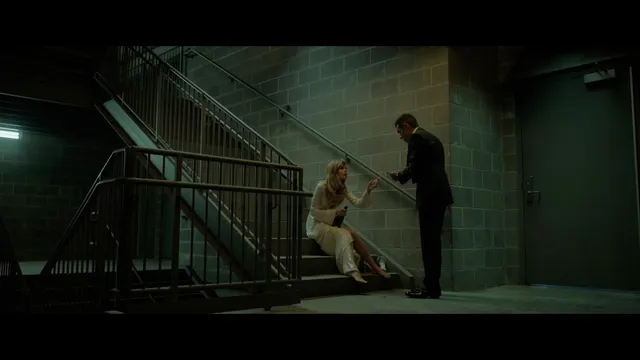 Samara Weaving sitting barefoot on stairs beside a man in a film scene.