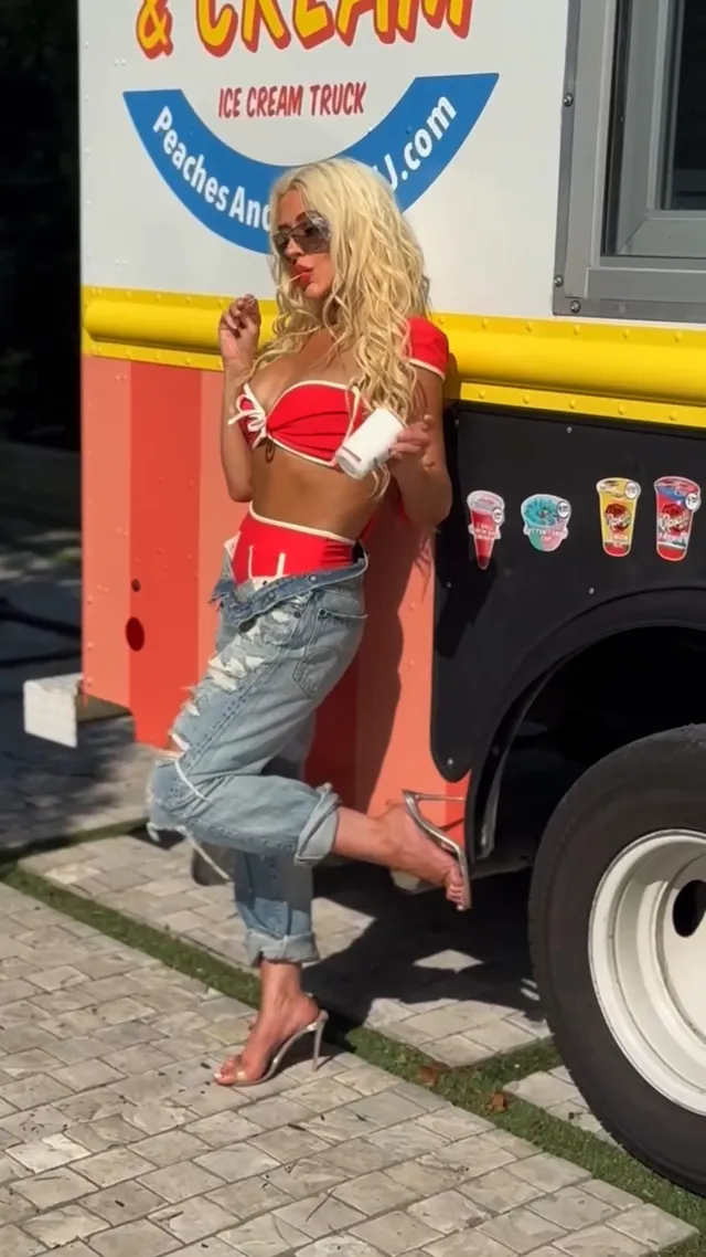 Christina Aguilera posing beside an ice-cream van with a heeled shoe raised.