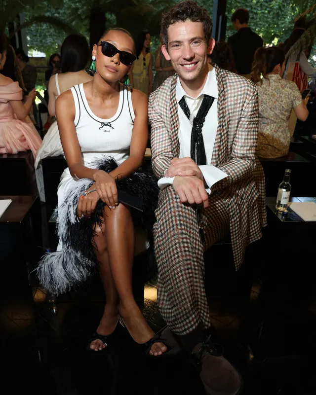Sophie Wilde sitting beside a man in a white dress and black heels.