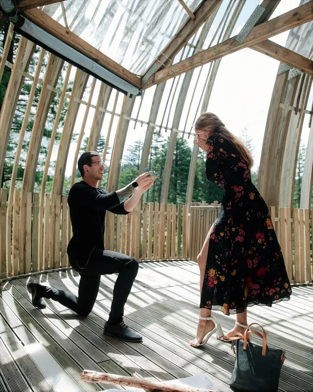 Debby Ryan standing in a floral dress and heels while a companion kneels nearby.