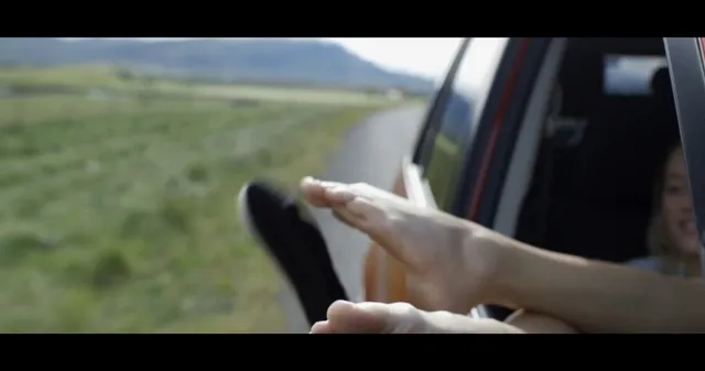 Maika Monroe showing a bare foot outside a vehicle window in a scene.