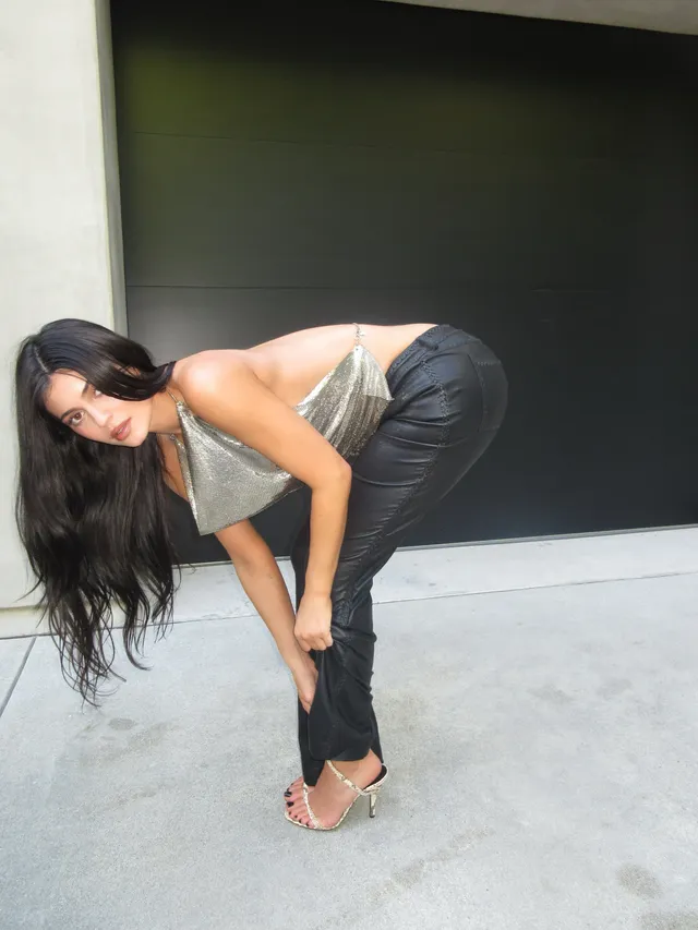 Kylie Jenner leaning forward in jeans and pale heels indoors.