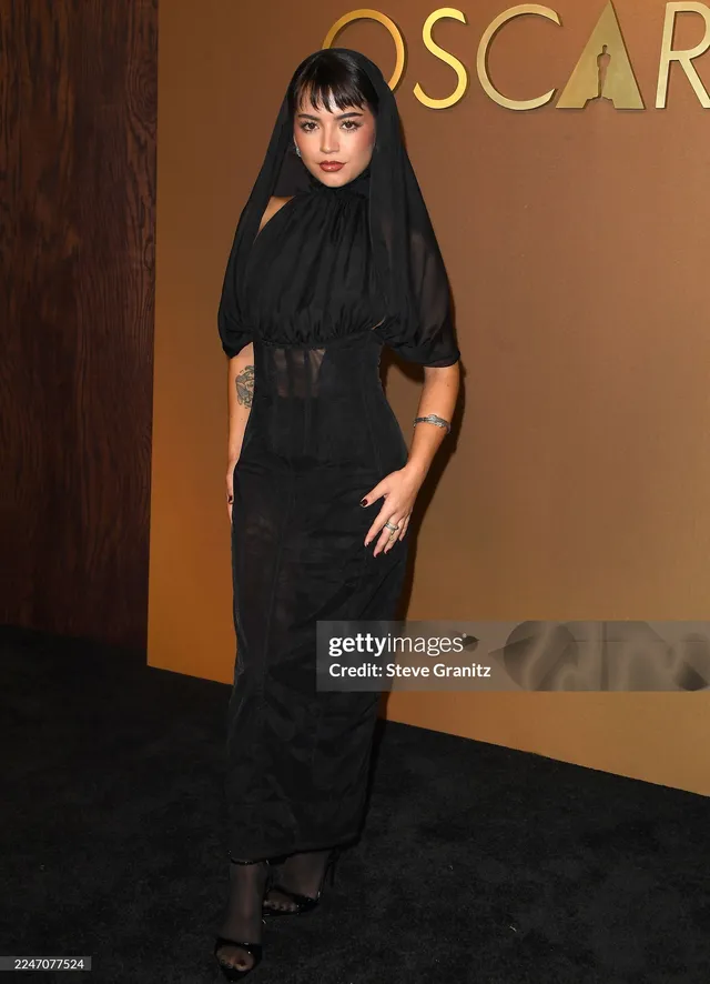Isabela Merced posing in a black gown and dark heeled sandals.