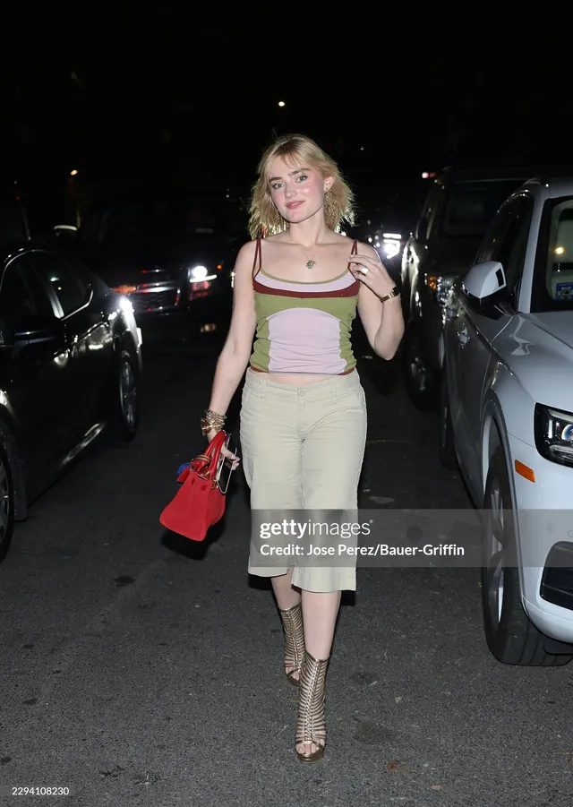 Meg Donnelly walking outside in a colorful top, pale skirt and metallic heels.