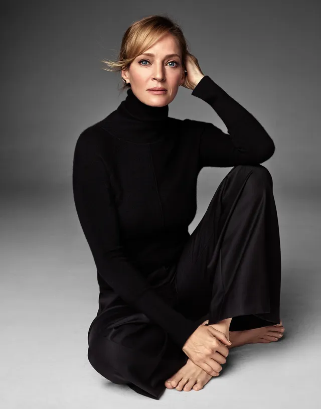 Uma Thurman sitting barefoot in a black outfit.