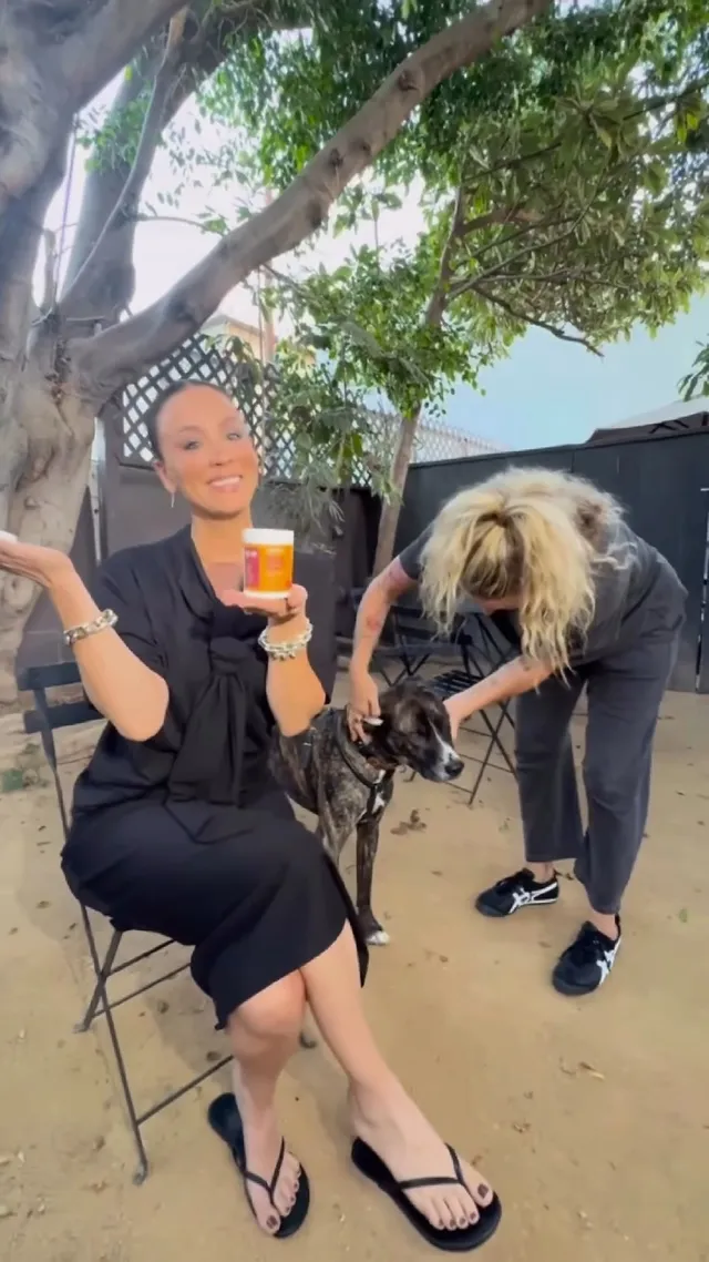 Kaley Cuoco sitting outdoors in a black dress and flip-flops.