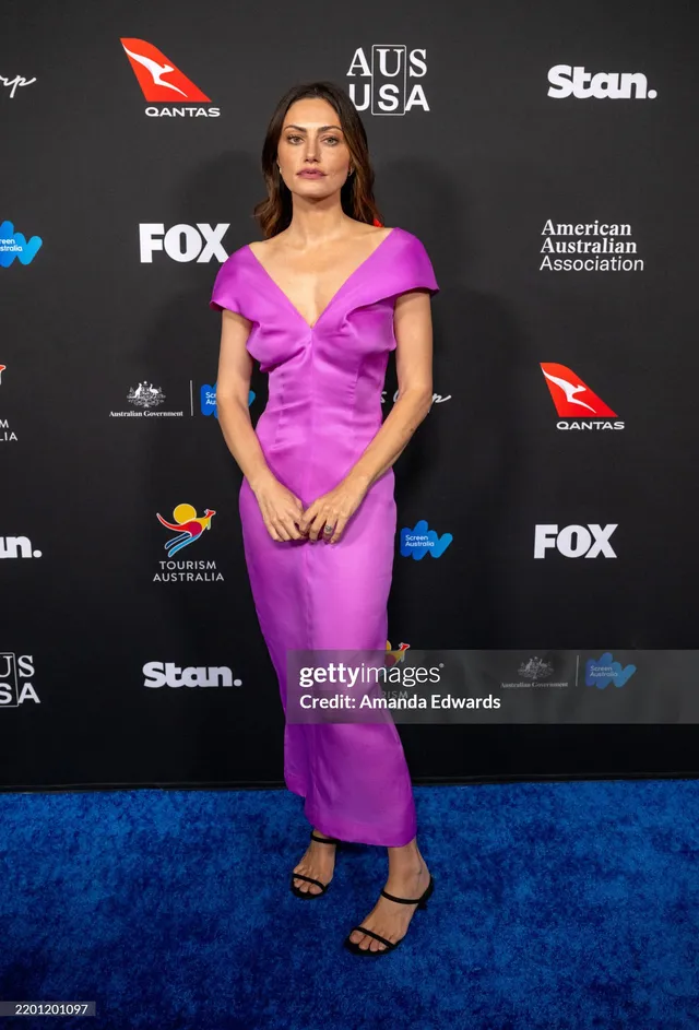 Phoebe Tonkin standing on a blue carpet in a purple dress.