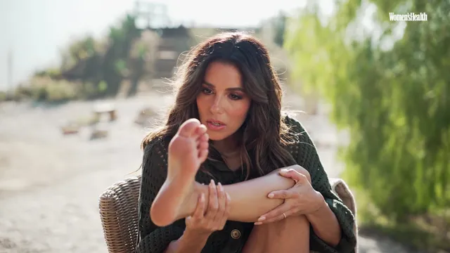 Eva Longoria holding her bare foot outdoors.