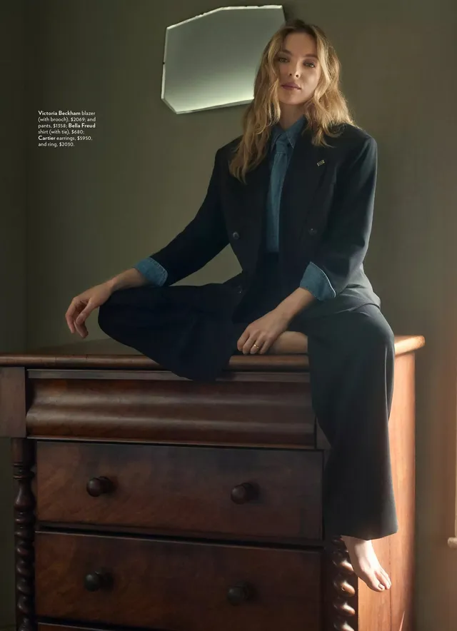 Jodie Comer sitting on a chest of drawers in a studio portrait.