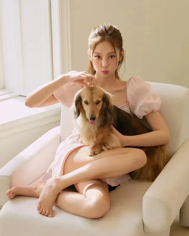 Jennie Kim sitting cross-legged and barefoot in a chair while holding a dog.