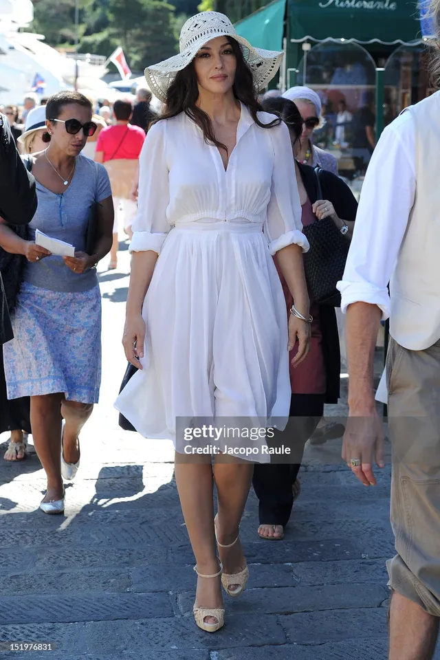 Monica Bellucci walking outdoors in a white dress and pale heels.