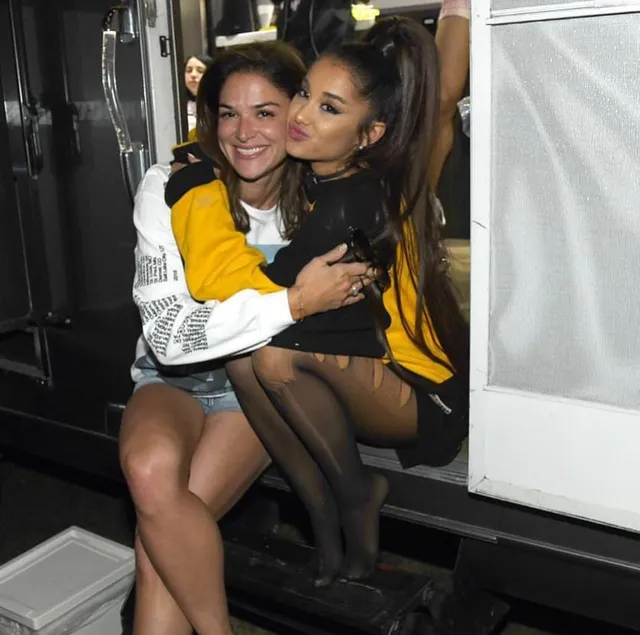 Ariana Grande sitting beside a guest in a backstage room.
