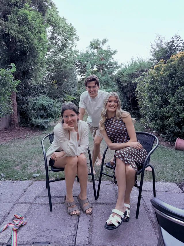 Eugenie Bouchard sitting outdoors with companions in white flat sandals and a dark patterned dress.
