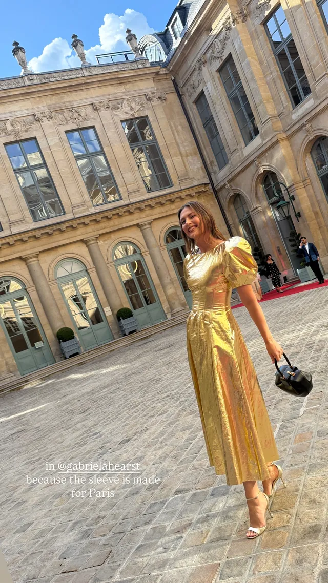 Maria Sharapova standing in gold heels and a long gold dress in a courtyard.