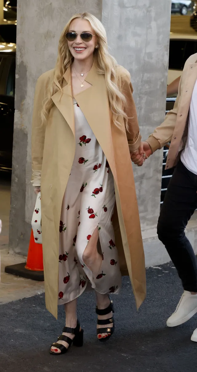 Lindsay Lohan wearing a long coat over a patterned dress outdoors.